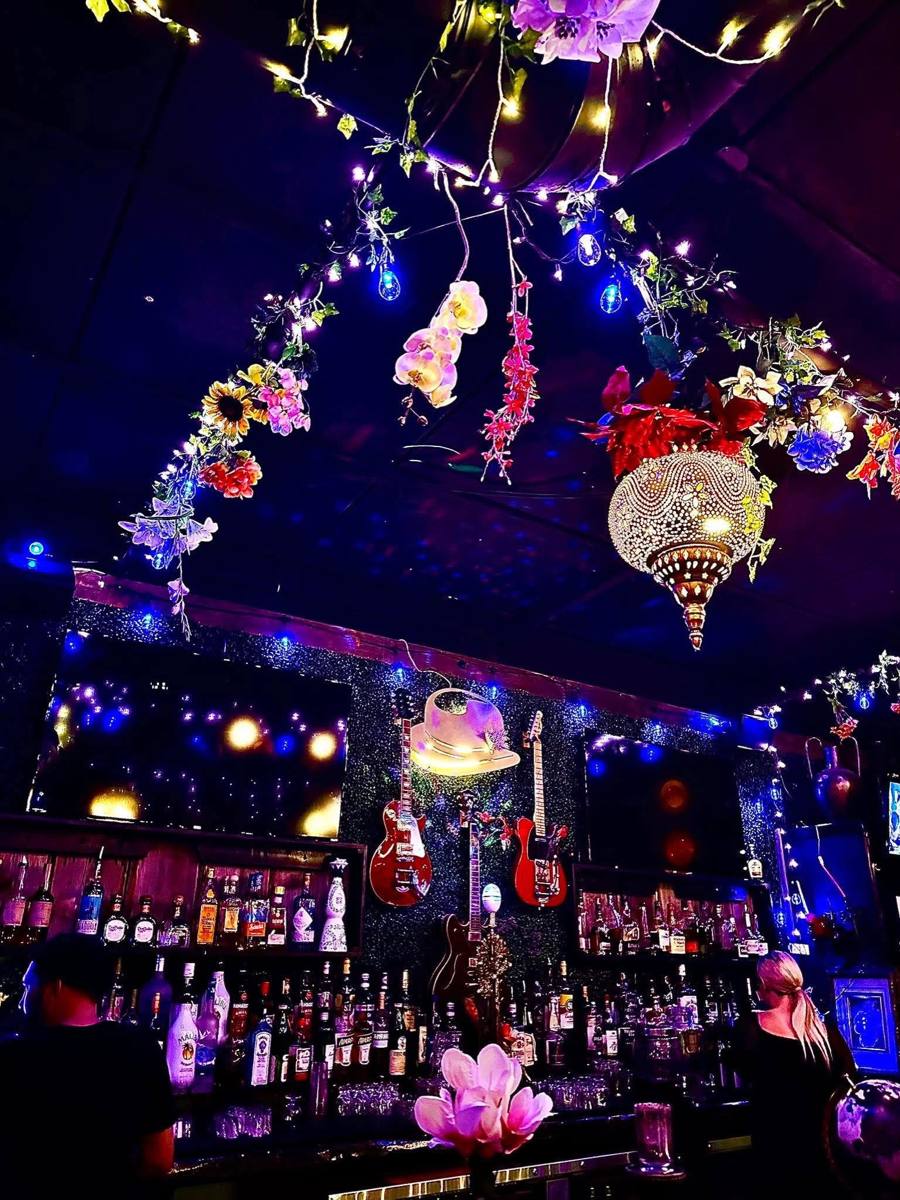 The Gibraltar bar seen from below: flowers and fairy lights strung across the ceiling, a beaded Moroccan lantern, guitars and a cream hat mounted on the back wall above rows of bottles.